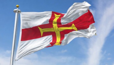 The flag of the Isle of Guernsey, Great Britain, flutters in the wind