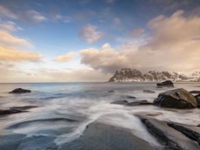 Smoothly polished rocks on Utakleiv beach in a dramatic cloudy atmosphere, snow-capped mountains in