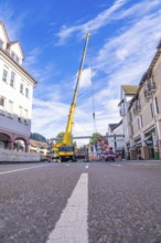 A lifting crane works on a road with zebra crossing in an urban environment, construction site