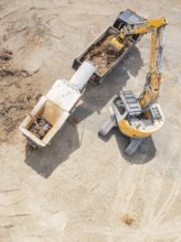 Aerial view of an excavator and a lorry working on a large construction site, demolition site,