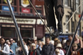 Feet balancing on rope, street performers and spectators at a high-wire acrobatics performance,