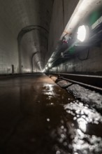 Long, dark tunnel with pools of water, concrete walls and light reflections, industrial atmosphere,