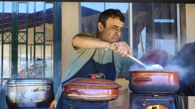 Chef Stelios, A man stirs in a pot on an open fire in a rustic kitchen while other pots stand next