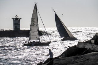 Sailing boat leaving the harbour of Scheveningen, lighthouse at the harbour entrance, Netherlands