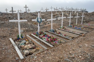 Crosses decorated with colourful flowers mark graves in a rocky area, cemetery, remote Arctic Inuit