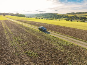 Black car on a rural country lane between fields in a vast rural landscape, car sharing, VW ID5,