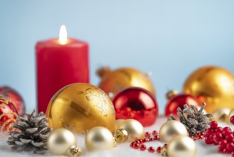 Burning candle with red and gold baubles and pine cones on artificial snow, festive atmosphere