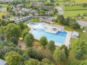 Aerial view of an outdoor swimming pool with several pools, slides and surrounding trees in a green