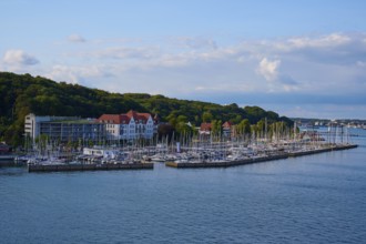 A picturesque harbour with many boats, surrounded by green nature and buildings under a blue sky