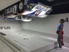 Visitor to the museum looks upwards at a Porsche 956 racing car hanging upside down under the