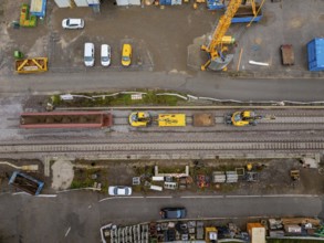 Aerial view of a construction site with a yellow train running on the tracks, next to it a road