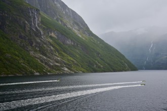 Two speedboats with groups of people travelling fast in the Geiranger Fjord, white waves are coming