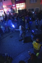 People gather at night on a street with glowing torches and security forces, carnival, Calw, Black