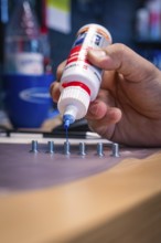 Hand applying blue liquid to screws on a workbench, Waldbike Manufaktur, bicycle workshop, Calw,