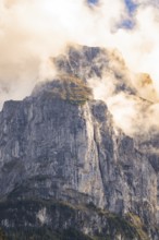 Impressive rock face rises into the sky, enveloped by light clouds, Lake Brienz, Switzerland,