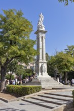 Historical monument with a tall statue in a green park area, Seville