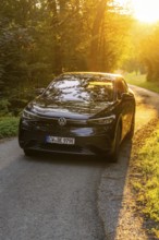 Car driving on a sunlit forest path, warm rays of light illuminate the road, electric car, VW ID5,