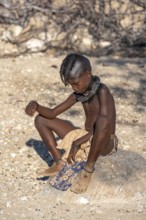 Himab girl sitting on a stone, traditional Himba village, Kaokoveld, Kunene, Namibia, Africa