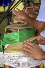 Hands playing several atabaque drums decorated with fabric being used during an Umbanda religious