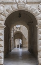 Stone arch above a narrow cobbled alley with antique lamps and historic stone walls, Altamura