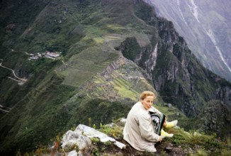 Female tourist sitting on the mountain Huayna Picchu with view of Machu Picchu, Peru, South America