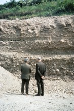 Two men, presumably geologists, looking at the rock face of a quarry, unspecified location1970