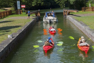 Canoes and a motorboat pass through a lock on a sunny river path, Sluza Paniewo, lock between the