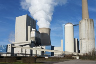 Large industrial plant with several chimneys and smoke in front of a blue sky, coal-fired power