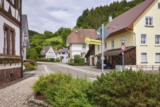 Carpooling point, multi-family houses, hilly landscape with coniferous forest, overcast sky with