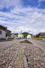 Traffic island, general architecture, Church of St Ulrich, hilly landscape with coniferous forest,