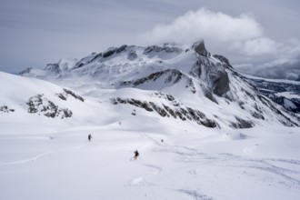 Ski tourers descending in a snow-covered mountain landscape, with the Sex des Molettes mountain