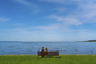 Woman and girl sitting on a bench in a meadow on the shore of the Szczecin Lagoon in the village of