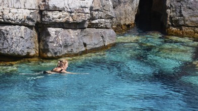 Palatia Beach, Palatia, A person swims in turquoise water in front of rocky surroundings and a