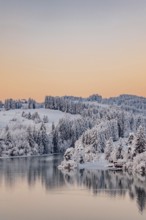 Dawn and sunrise at the wintry Forggensee in a snow-covered winter landscape in the foothills of