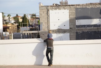 Child sitting on father's shoulders watching building site work, Fuerteventura, Canary Islands,