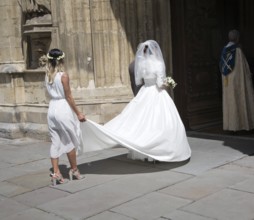 Bride wearing white wedding dress with her bridesmaid as they enter Bath Abbey church, Bath,