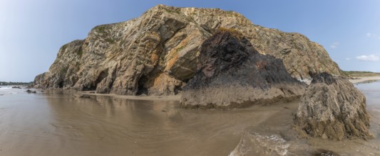 A beach with a rocky cliff in the background. The water is calm and the reflection of the cliff is