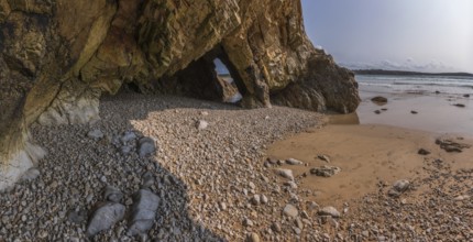 A rocky beach with a large rock formation and a small cave. The rocks are scattered all over the