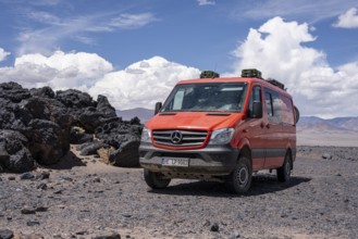 Red off-road vehicle standing on stony ground under blue sky, Argentina, volcanoes, lava field,