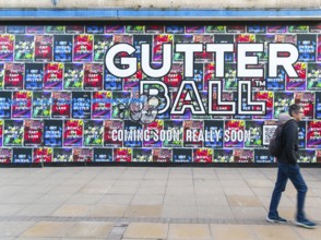 Person waking past posters on shopfront advertising Gutter Ball ten pin bowling attraction,