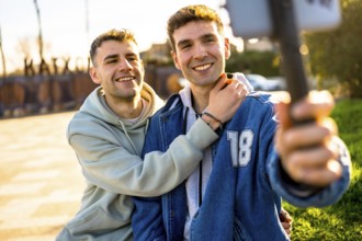 Two men in love are hugging and taking a selfie with a smartphone, enjoying a sunny day outdoors