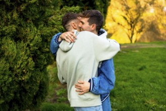 Two men hugging each other tightly in a park, enjoying a tender moment of love and connection