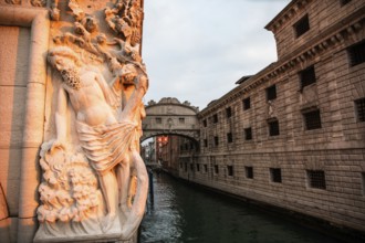 Morning light falls on a stone sculpture of an ancient deity, behind the Bridge of Sighs or Ponte