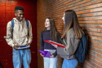 Happy diverse college students chatting and laughing together in university hallway, enjoying their