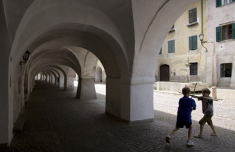 Italy S-Tyrol Neumarkt Laubengasse with view to the alleyway fountain and playing boys