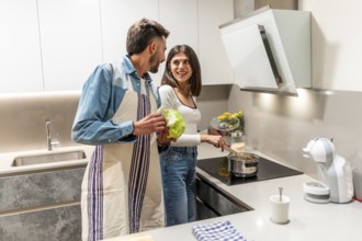 Happy couple wearing aprons, preparing healthy meal together in their modern kitchen, enjoying