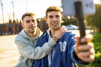 Two men in love embracing each other while capturing a joyful selfie with a smartphone mounted on a