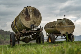 Two dilapidated water tank trailers standing in a field under a cloudy sky, Lower Saxony, Germany,