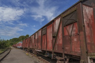 Long goods train with red wagons on tracks under a partly cloudy blue sky, bochum, North