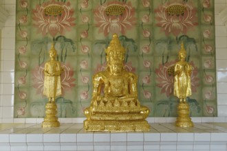 Three golden statues on a pedestal in front of ornately decorated walls inside the temple, penang,